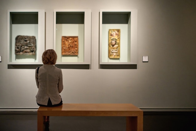 Achteraanzicht van een vrouw die in een kunstgalerie zit voor kleurrijke schilderijen
