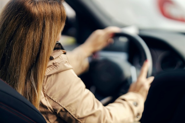 Achteraanzicht van een vrouw die in haar auto rijdt en aan de telefoon praat