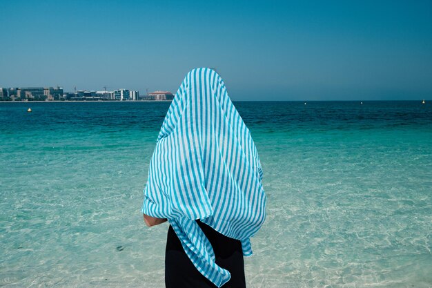 Achteraanzicht van een vrouw die naar de zee loopt in Palm Jumeirah Dubai Een vrouw in een sjaal en jurk geniet van de zoute zeelucht
