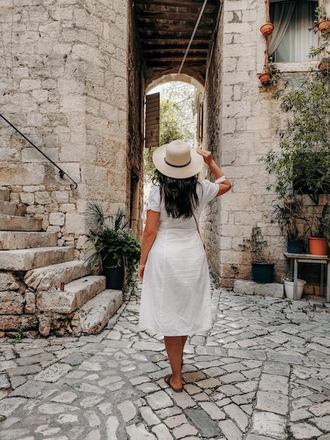 Achteraanzicht van een vrouw in een witte jurk die door de idyllische oude straat in de stad Trogir, Kroatië loopt.