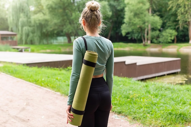 Achteraanzicht van een vrouw in het park in de zomer met een groene gymmat achter haar rug