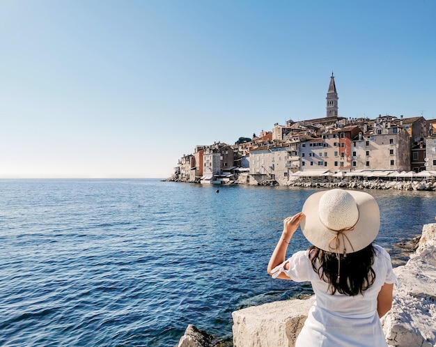 Achteraanzicht van een vrouw zittend op een rots aan zee, kijkend naar de pittoreske badplaats Rovinj, Kroatië.