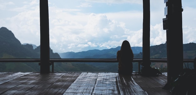 Achteraanzicht van een vrouwelijke reiziger die zit en kijkt naar een prachtig uitzicht op de bergen en de natuur