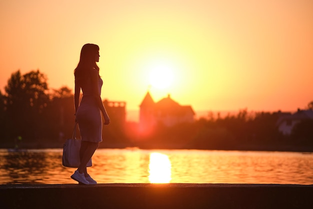 Achteraanzicht van eenzame vrouw die alleen staat op de oever van het meer op warme avond. Eenzaamheid en ontspannen in de natuur concept.