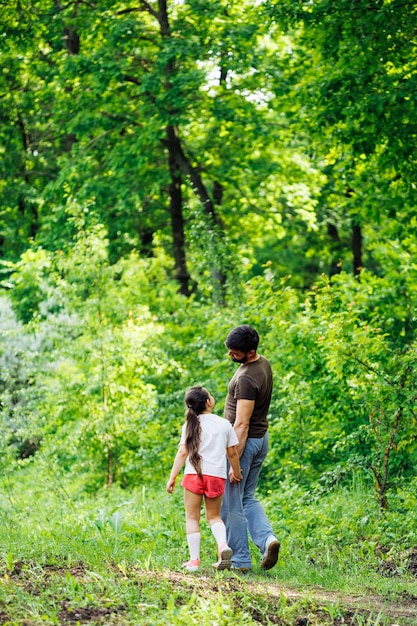 Achteraanzicht van familie wandelen in parkbos rond bomen pratend plezier Zomeractiviteiten reizen Verticaal