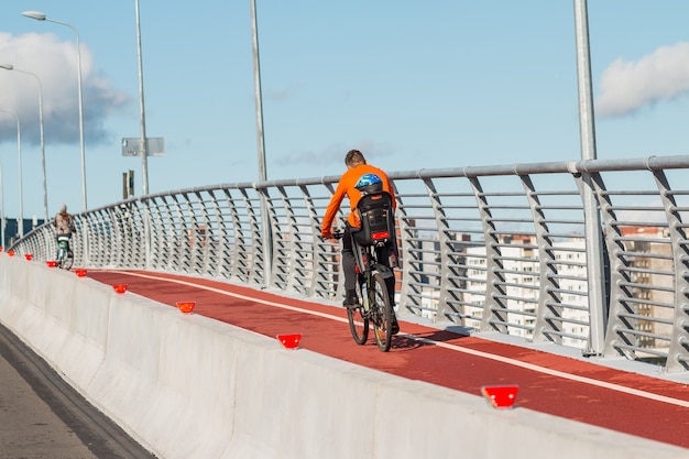 Achteraanzicht van fietser met kinderstoel en baby. familie fietsen in de stad op de brug. vader met kind paardrijden fiets buitenshuis. actieve sport vrije tijd.