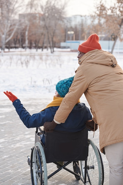 Achteraanzicht van gehandicapte vrouw in rolstoel wandelen in de winterdag met assistent