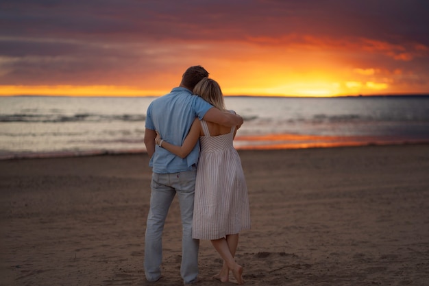 achteraanzicht van gelukkige paar knuffelen op het strand bij zonsondergang