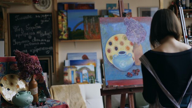 Achteraanzicht van jong schildersmeisje in schort schilderij stilleven op canvas in artclass