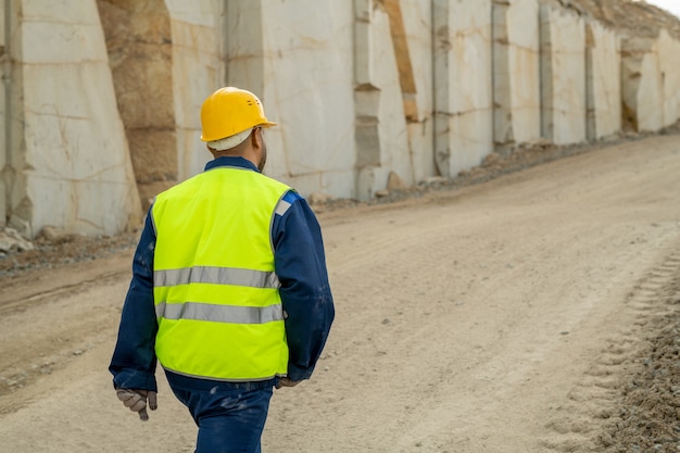 Achteraanzicht van jonge bouwer in werkkleding die langs de muur van een onafgewerkt gebouw beweegt