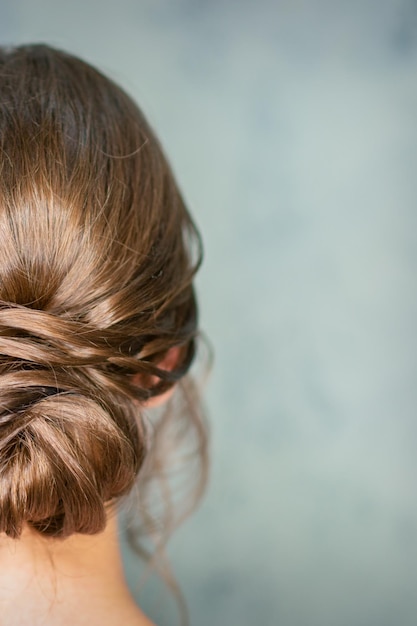 Achteraanzicht van jonge brunette vrouw met mooi midden broodje kapsel op grijze achtergrond.