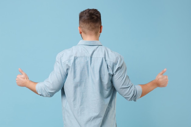 Foto achteraanzicht van jonge kerel 20s in casual shirt poseren geïsoleerd op pastel blauwe muur achtergrond studio portret. mensen oprechte emoties levensstijl concept. bespotten kopie ruimte. duimen omhoog laten zien.