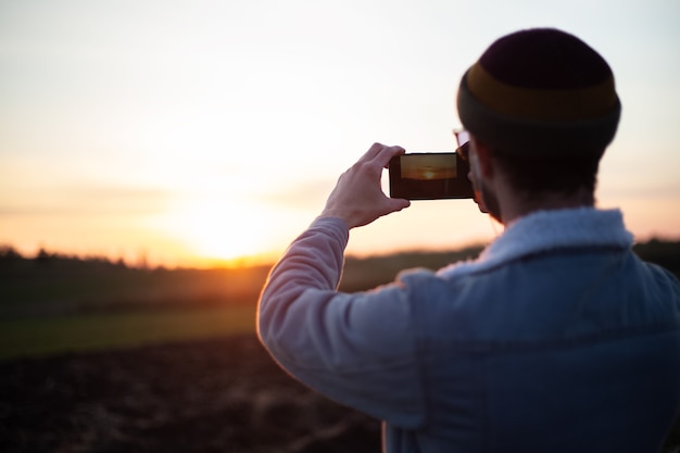 Achteraanzicht van jonge kerel fotograferen van zonsondergang door smartphone