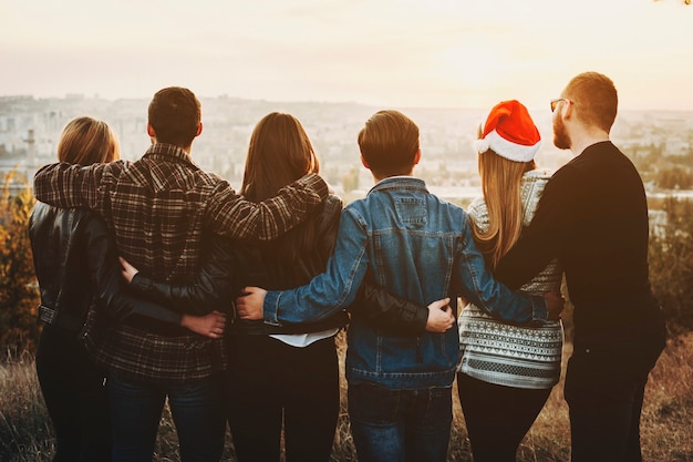 Achteraanzicht van jonge mannen en vrouwen die elkaar knuffelen en kijken naar de moderne stad terwijl ze samen kerstmis vieren