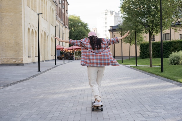 Achteraanzicht van jonge stijlvolle tiener die buiten op skateboard rijdt