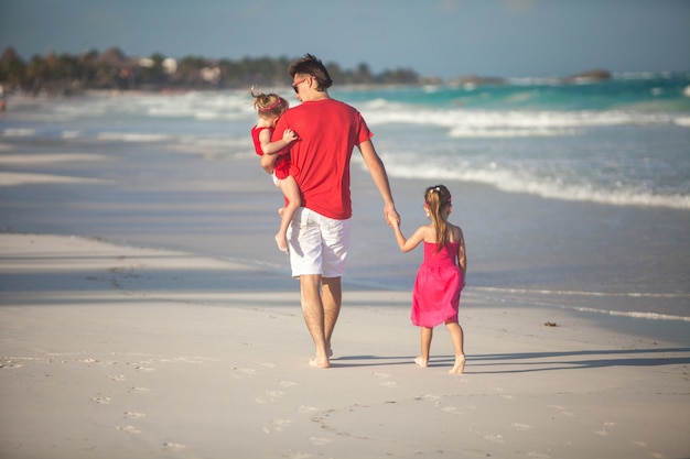 Achteraanzicht van jonge vader en zijn schattige dochters wandelen langs de zee