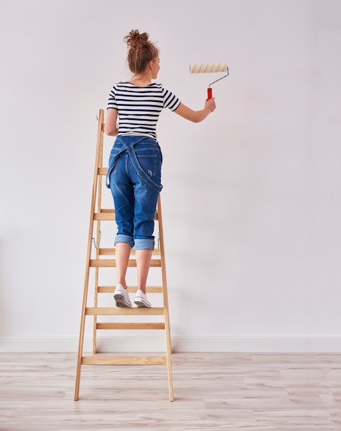 Achteraanzicht van jonge vrouw met verfroller schilderij muur