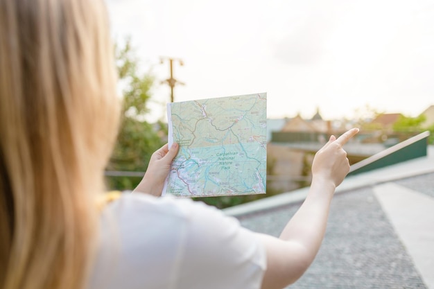 Foto achteraanzicht van jonge vrouwelijke toerist kijkt aandachtig naar de stadsplattegrond