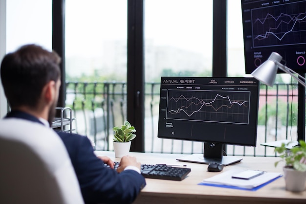 Achteraanzicht van knappe jonge, bebaarde zakenman die op zijn computer typt. Grafische computermonitor.