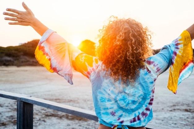 Achteraanzicht van krullend haar vrouw uitgestrekte armen en genieten van een gelukkige levensstijl en vrijetijdsvakantie in de buitenlucht tegen een prachtige zonnige zonsondergang Concept van mensen en reizen levensstijl Vrouwelijke opening armen