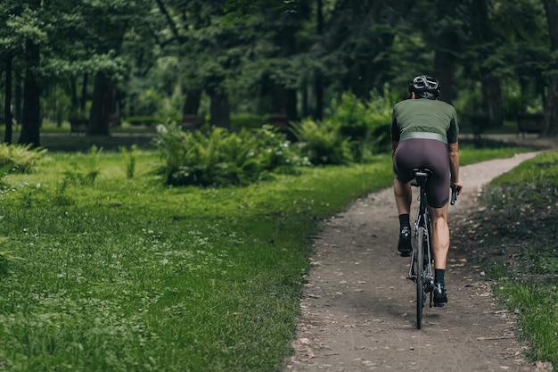 Achteraanzicht van man met gespierde benen zwarte fiets rijden op frisse lucht. Jonge kerel die actieve kleding en veiligheidshelm draagt. Outdoor training voor een gezonde levensstijl.