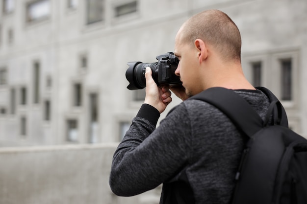 Achteraanzicht van mannelijke fotograaf die foto's maakt met moderne professionele dslr-camera over betonnen gebouwachtergrond