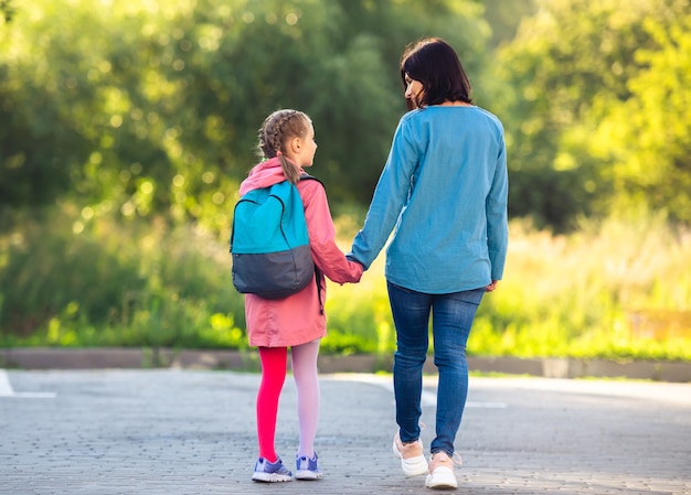 Achteraanzicht van moeder en schoolmeisje hand in hand wandelen langs de parkeerplaats