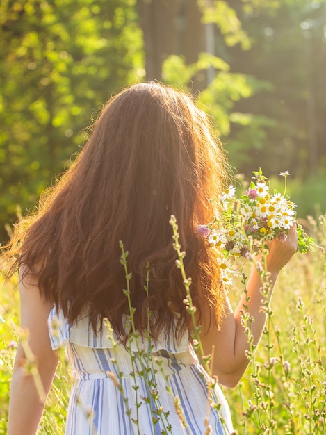 Achteraanzicht van mooie jonge vrouw lopen onder wilde bloemen op zonnige zomerdag. Concept van de vreugde van communiceren met de zomeraard