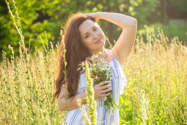 Achteraanzicht van mooie jonge vrouw lopen onder wilde bloemen op zonnige zomerdag. Vreugde om te communiceren met de zomerse natuur