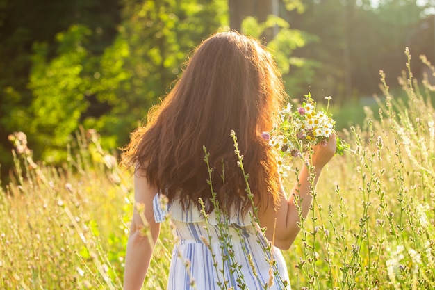 Achteraanzicht van mooie jonge vrouw lopen onder wilde bloemen op zonnige zomerdag