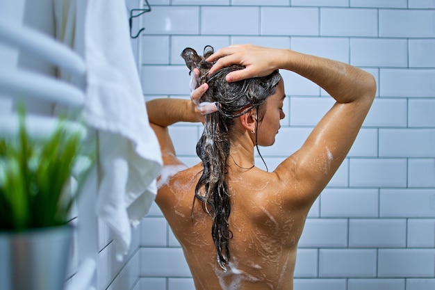 Achteraanzicht van naakte vrouw haar met shampoo wassen tijdens het nemen van een douche
