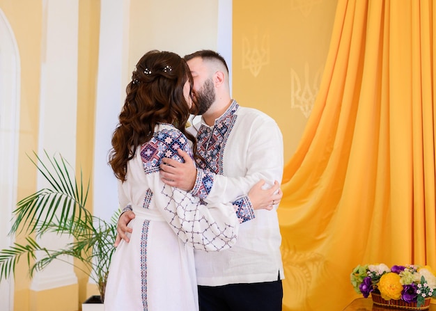 Achteraanzicht van pasgetrouwden die in etnische outfit met kleurrijk patroon elkaar knuffelen en kussen tijdens het registreren van het burgerlijk huwelijk in de ceremonieruimte