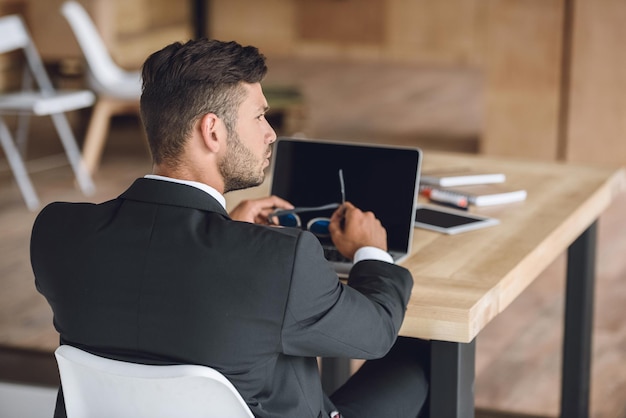 Achteraanzicht van peinzende zakenman zittend op de werkplek met laptop op kantoor