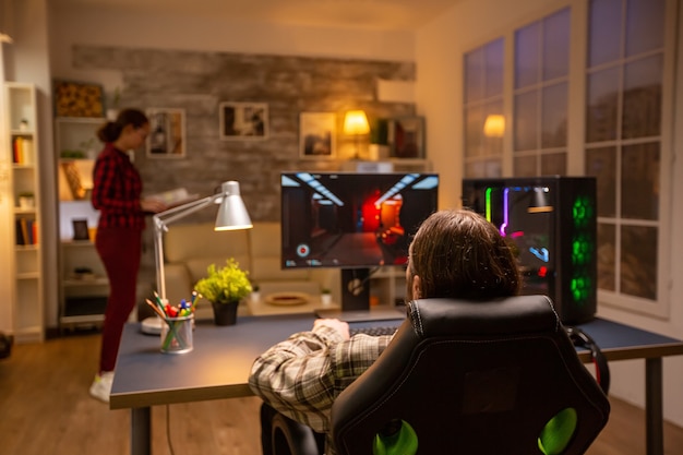Foto achteraanzicht van professionele videogamer die 's avonds laat in de woonkamer op een krachtige pc speelt.