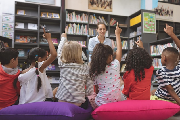 Achteraanzicht van schoolkinderen die de hand in de bibliotheek steken om een vraag te beantwoorden