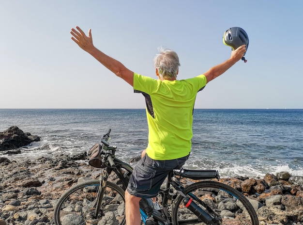 Achteraanzicht van senior man buitenshuis met open armen fietsen op zee genietend van vrijheid en een gezonde levensstijl