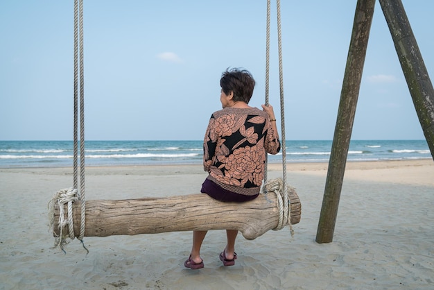 Achteraanzicht van senior vrouw zittend op een houten plank schommel met uitzicht op de zee