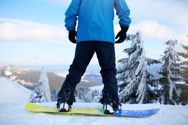 Achteraanzicht van snowboarder benen op zijn board voor backcountry freeride sessie in het bos Man's voeten in laarzen gemonteerd in moderne snowboard fast flow bindingen vast met riemen Ruiter in skiresort