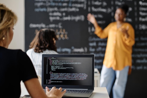 Achteraanzicht van student die codes schrijft op laptop die tijdens de les aan een bureau zit