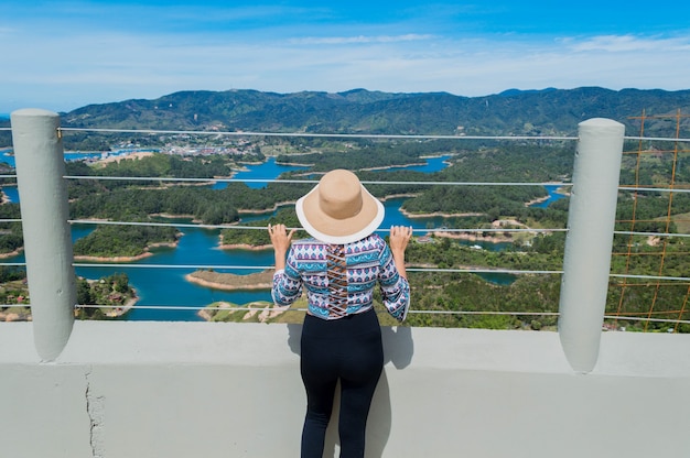 Achteraanzicht van toeristische vrouw met hoed die de natuur in Guatape Colombia overweegt van Penol-steen