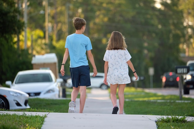 Achteraanzicht van twee jonge tienerkinderen, meisje en jongen, broer en zus die samen op landelijke straat lopen op een heldere zonnige dag Vakantietijdconcept