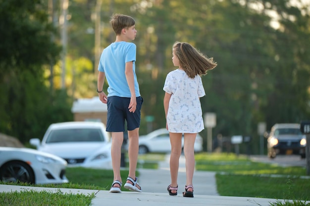 Achteraanzicht van twee jonge tienerkinderen, meisje en jongen, broer en zus die samen op landelijke straat lopen op een heldere zonnige dag vakantietijdconcept