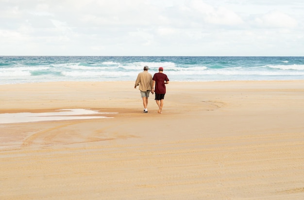 Achteraanzicht van twee vrienden die op een strand lopen en praten met de oceaan als achtergrond