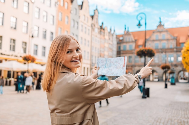 Achteraanzicht van verloren jonge vrouwelijke toerist die een papieren kaart vasthoudt op het centrale plein in de oude stad van gdansk