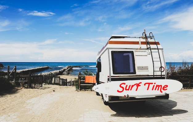 Achteraanzicht van vintage camper geparkeerd op het strand tegen een prachtig schilderachtig uitzicht Caravan van surfer met een surfplank op de rug Nomadisch leven concept van surfer wachten op betere golven Surf tijd tekst