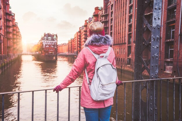 Achteraanzicht van volwassen vrouw toerist met rugzak genieten van zonsondergang op de brug in Speicherstadt