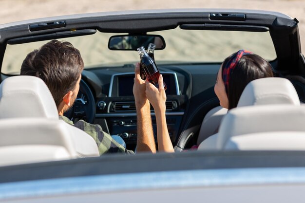 Achteraanzicht van vriend en vriendin die juichen met colaflessen die cabriolet rijden