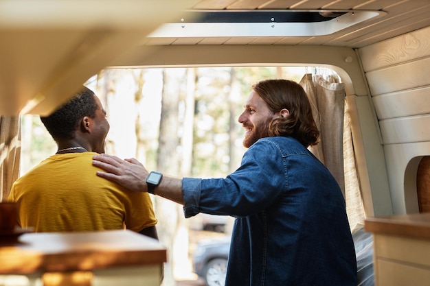 Foto achteraanzicht van vrienden die met elkaar praten terwijl ze in de camper zitten tijdens het kamperen in het bos