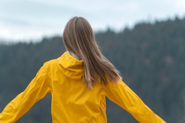 Achteraanzicht van vrouw met bruin haar draagt gele regenjas buiten Toeristenmeisje op bergenachtergrond