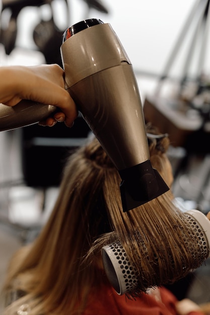 Achteraanzicht van vrouw met lang donker haar zittend in schoonheidssalon onherkenbaar schoonheidsspecialiste droog haar